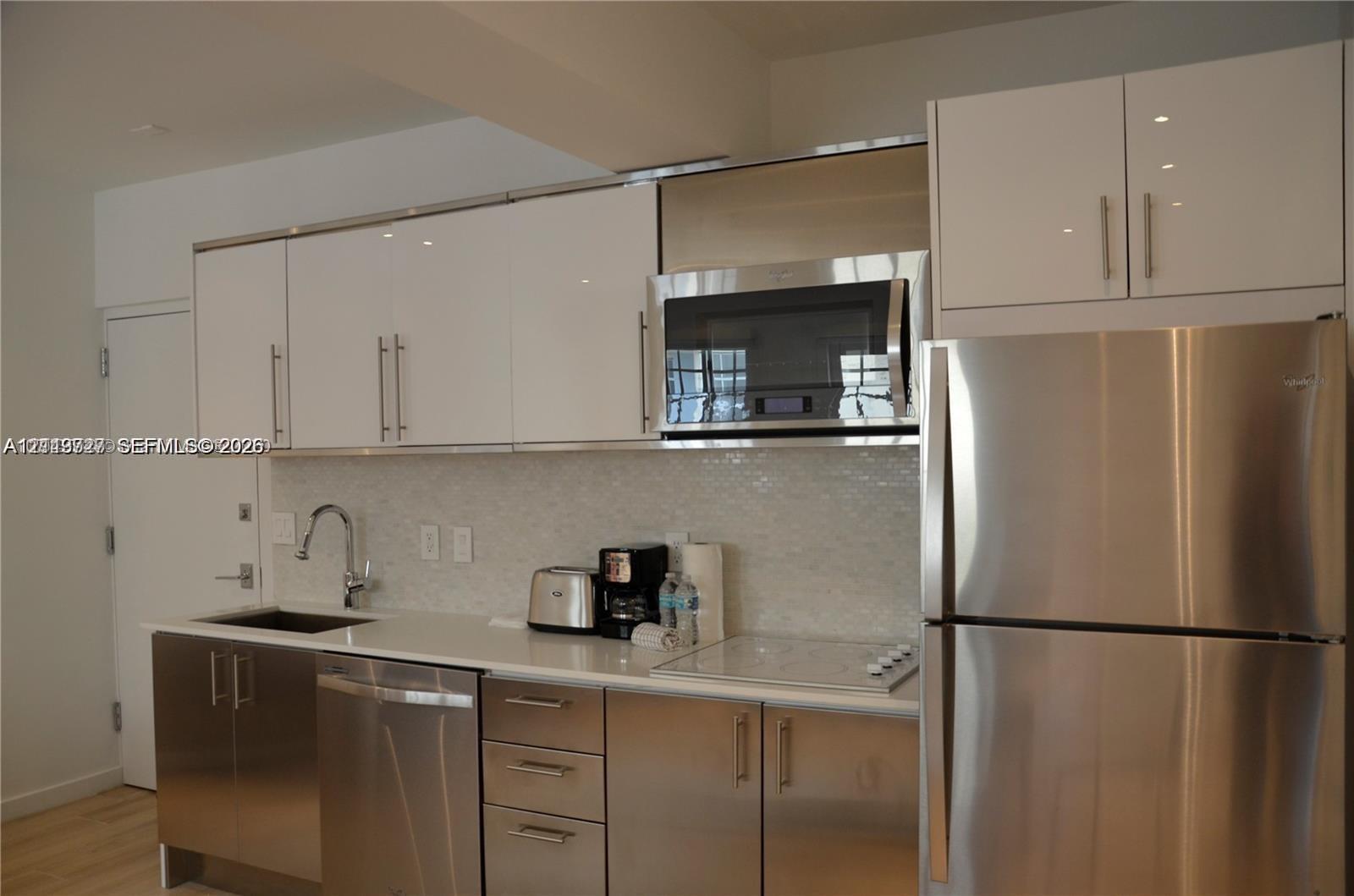 Kitchen featuring high-gloss white upper cabinetry, stainless steel lower cabinetry, solid-surface countertops, mosaic tile backsplash, and stainless steel appliances