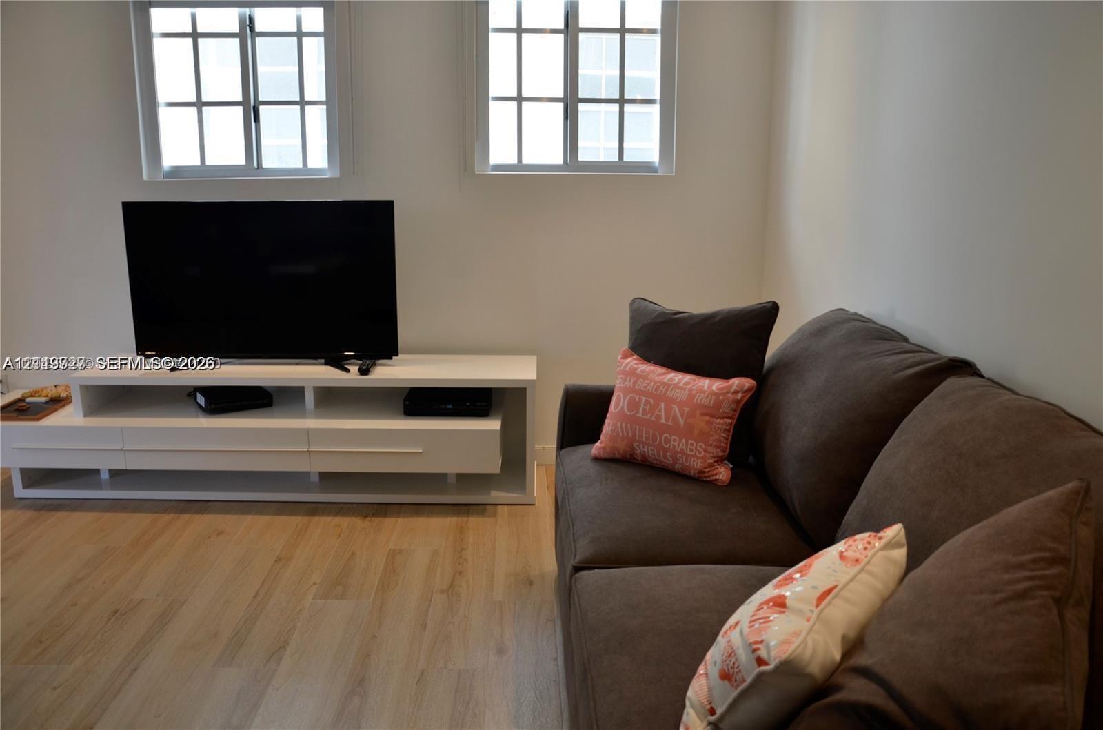 Light-toned wood-finish flooring, two dual-pane windows with grid detailing, and a white built-in media console Light-toned wood-finish flooring, two dual-pane windows with grid detailing, and a white built-in media console