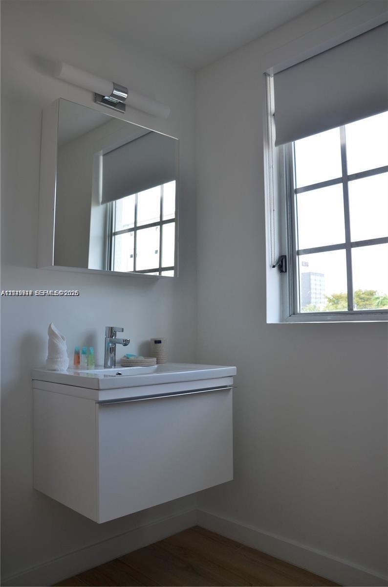 Wall-mounted floating vanity with a integrated basin and chrome single-lever faucet, accompanied by a matching mirrored medicine cabinet, linear wall-mounted lighting fixture, and window with a grid pattern