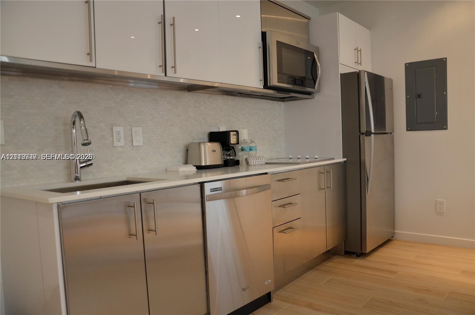 Kitchen featuring flat-panel white cabinetry, stainless steel appliances, stone-finish countertops, high-arc faucet, and wood-finish flooring Kitchen featuring flat-panel white cabinetry, stainless steel appliances, stone-finish countertops, high-arc faucet, and wood-finish flooring