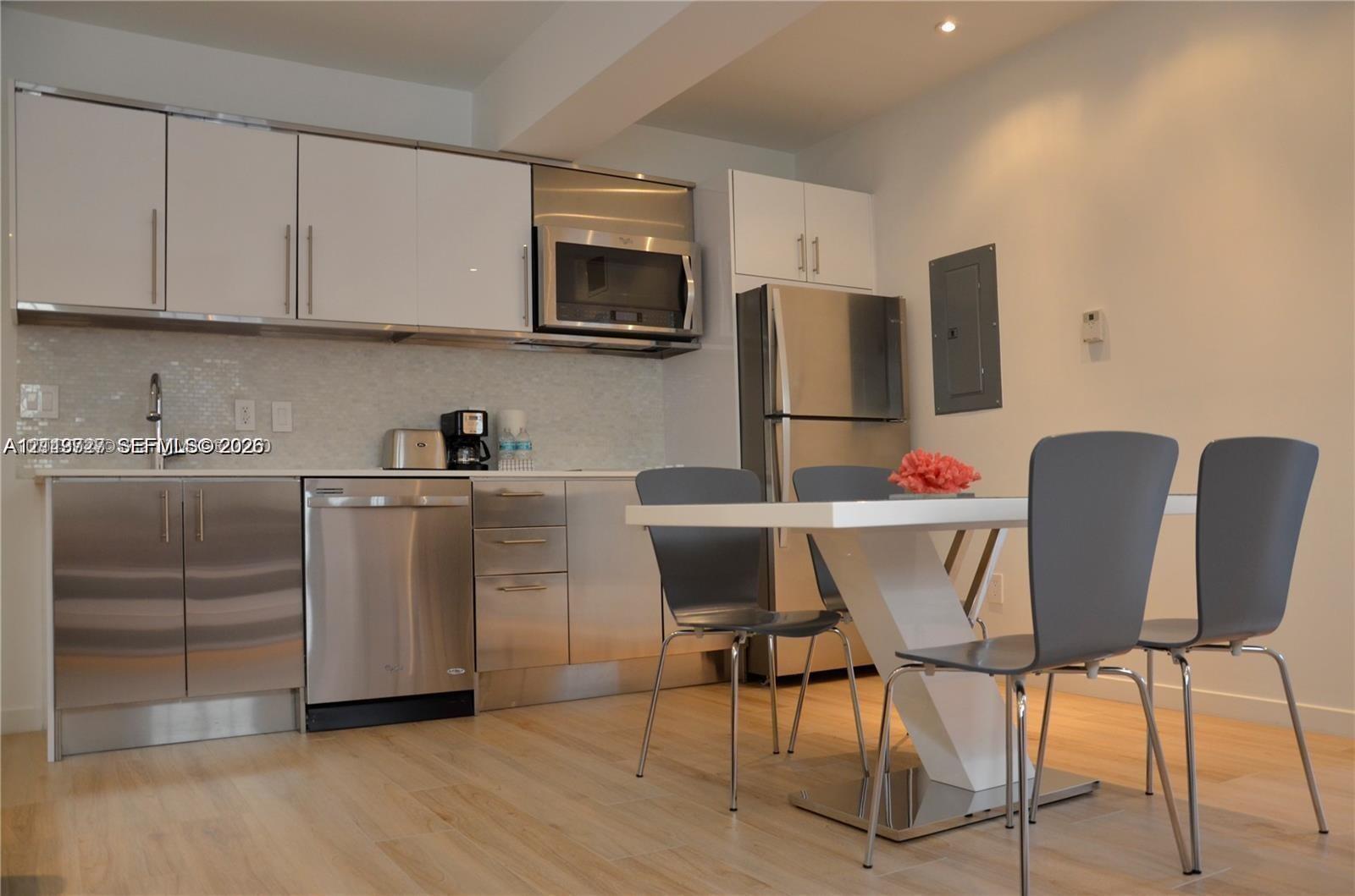 Kitchen featuring high-gloss white upper cabinetry, stainless steel lower cabinetry, built-in stainless steel microwave, integrated dishwasher, and light-toned wood-finish flooring
