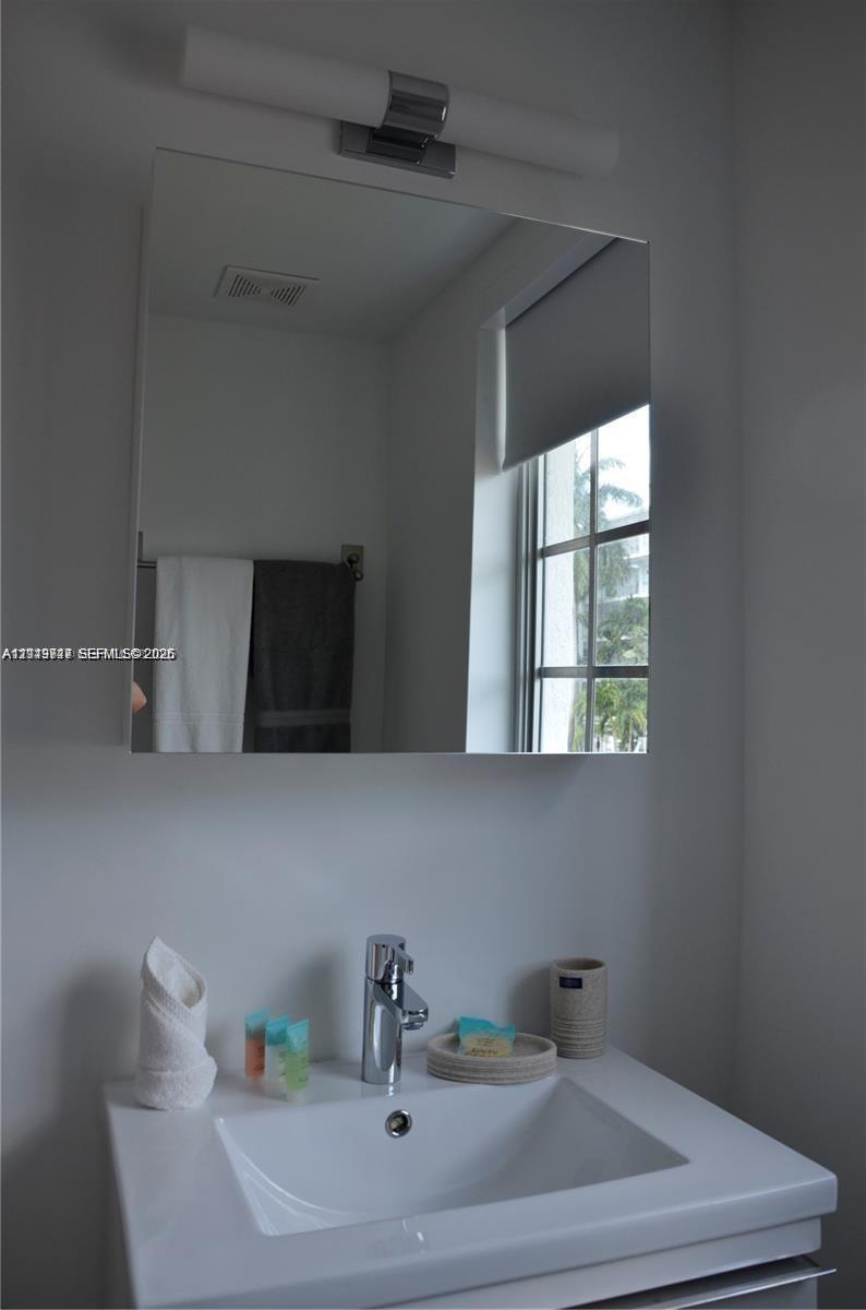 Wall-mounted rectangular mirror featuring a chrome-finished light fixture, integrated sink with a single-handle faucet, and built-in towel hardware