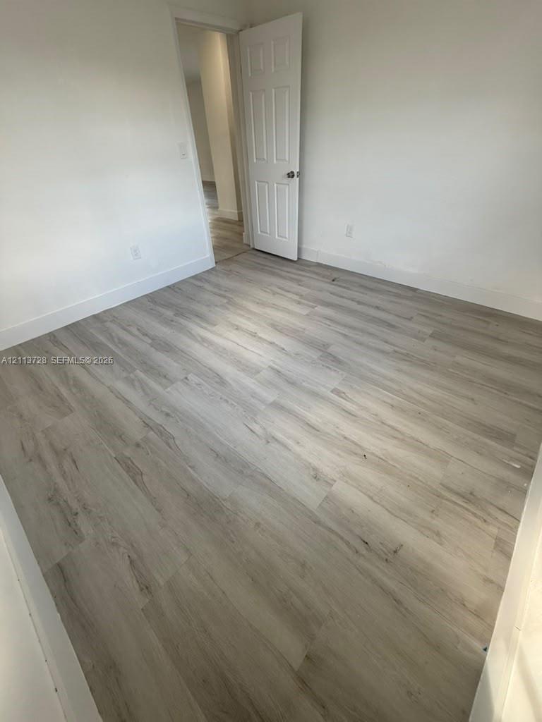 Room featuring wood-finish flooring, neutral walls, and a six-panel door