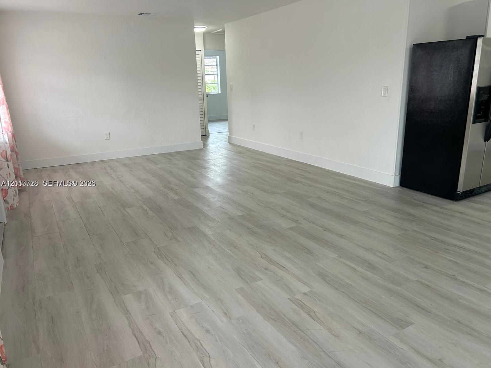 Open-concept interior featuring light-toned wood-finish flooring, neutral walls, and a stainless steel refrigerator Open-concept interior featuring light-toned wood-finish flooring, neutral walls, and a stainless steel refrigerator