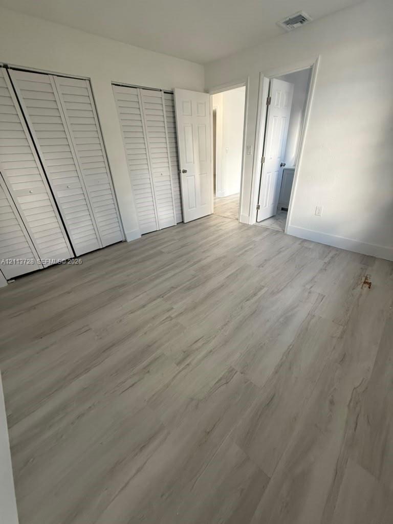 Interior space featuring wood-finish flooring, two sets of white louvered-style closet doors, and multi-panel interior doors