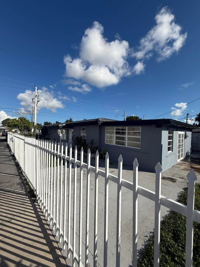 Single-story exterior featuring a white metal picket fence, paved concrete driveway, multi-pane windows, and dual-pane glass entry doors Single-story exterior featuring a white metal picket fence, paved concrete driveway, multi-pane windows, and dual-pane glass entry doors