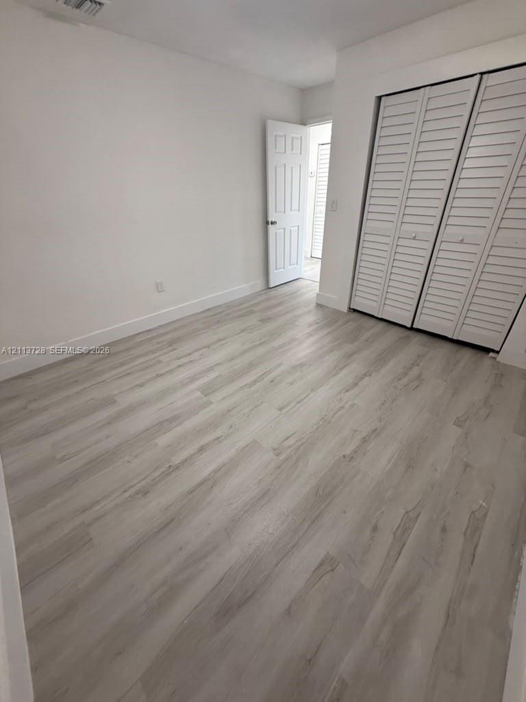 Interior room featuring wood-finish flooring, white walls, and a closet with white louvered bi-fold doors