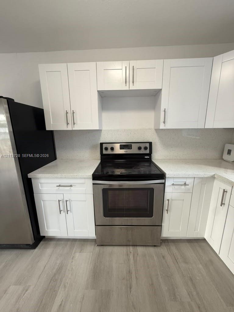 Kitchen featuring white shaker-style cabinetry, speckled stone-composite countertops, stainless steel electric range, and wood-finish flooring