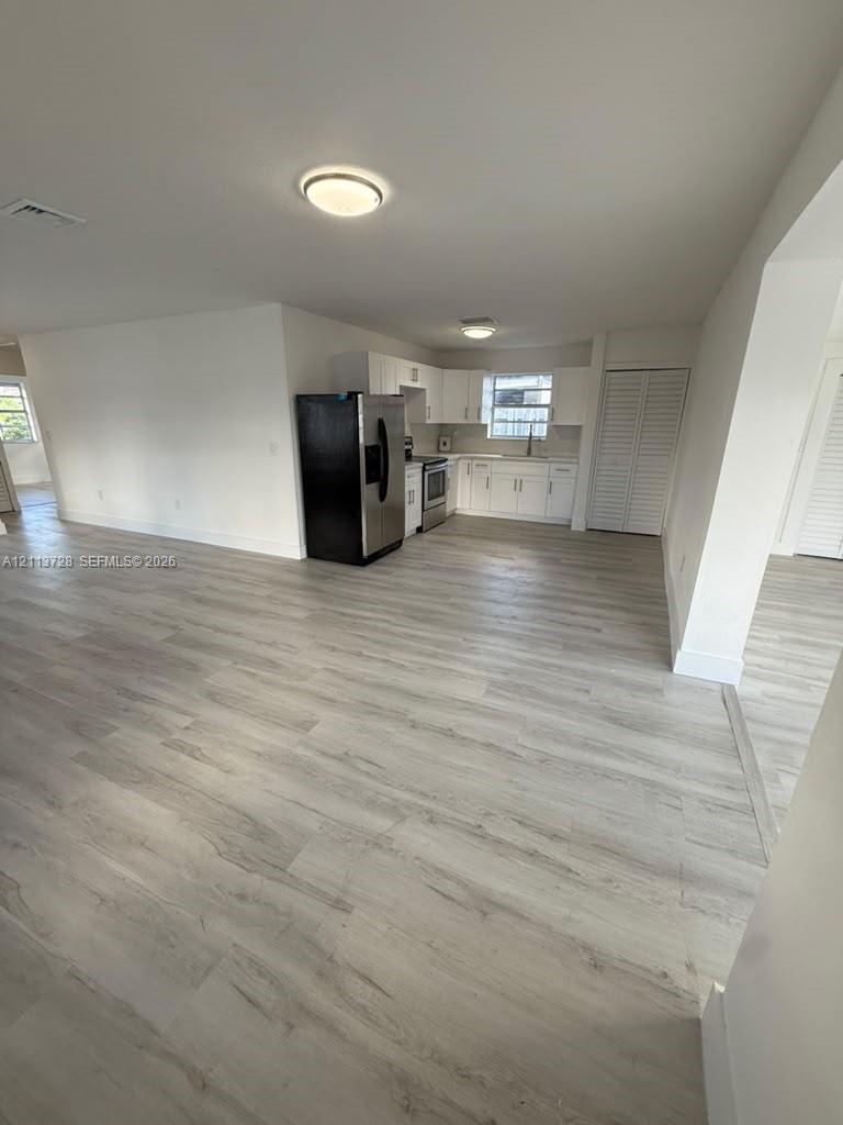 Kitchen featuring white shaker-style cabinetry, stainless steel side-by-side refrigerator, smooth-top range, and wood-finish flooring
