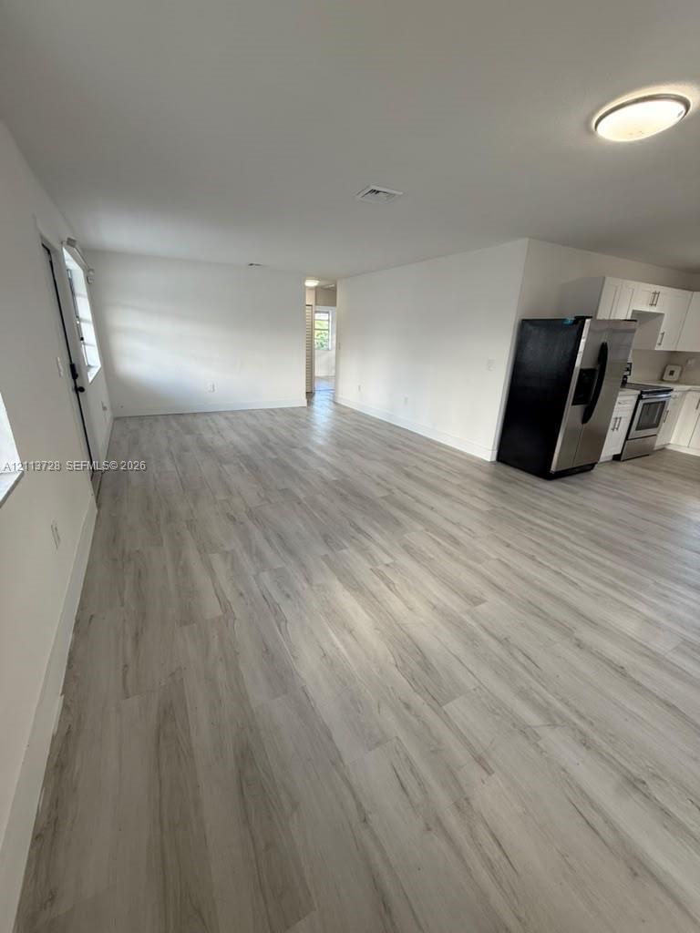 Open-concept interior featuring light wood-finish flooring, white cabinetry, stainless steel appliances, and flush-mount ceiling lighting Open-concept interior featuring light wood-finish flooring, white cabinetry, stainless steel appliances, and flush-mount ceiling lighting