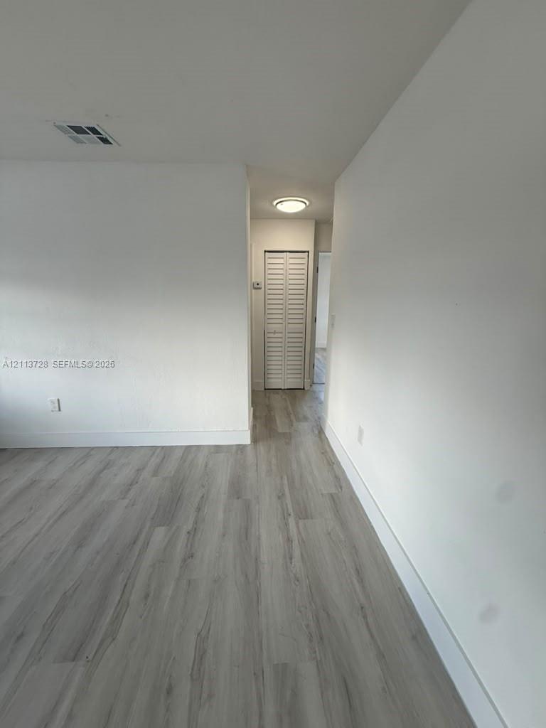 Wood-finish flooring, neutral walls, and a closet with white louvered doors