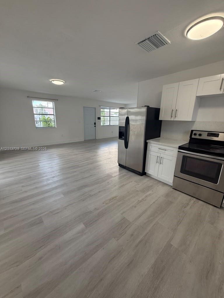 Kitchen featuring shaker-style white cabinetry, stone-finish countertops, and stainless steel appliances, set against wood-finish flooring and flush-mount ceiling lighting