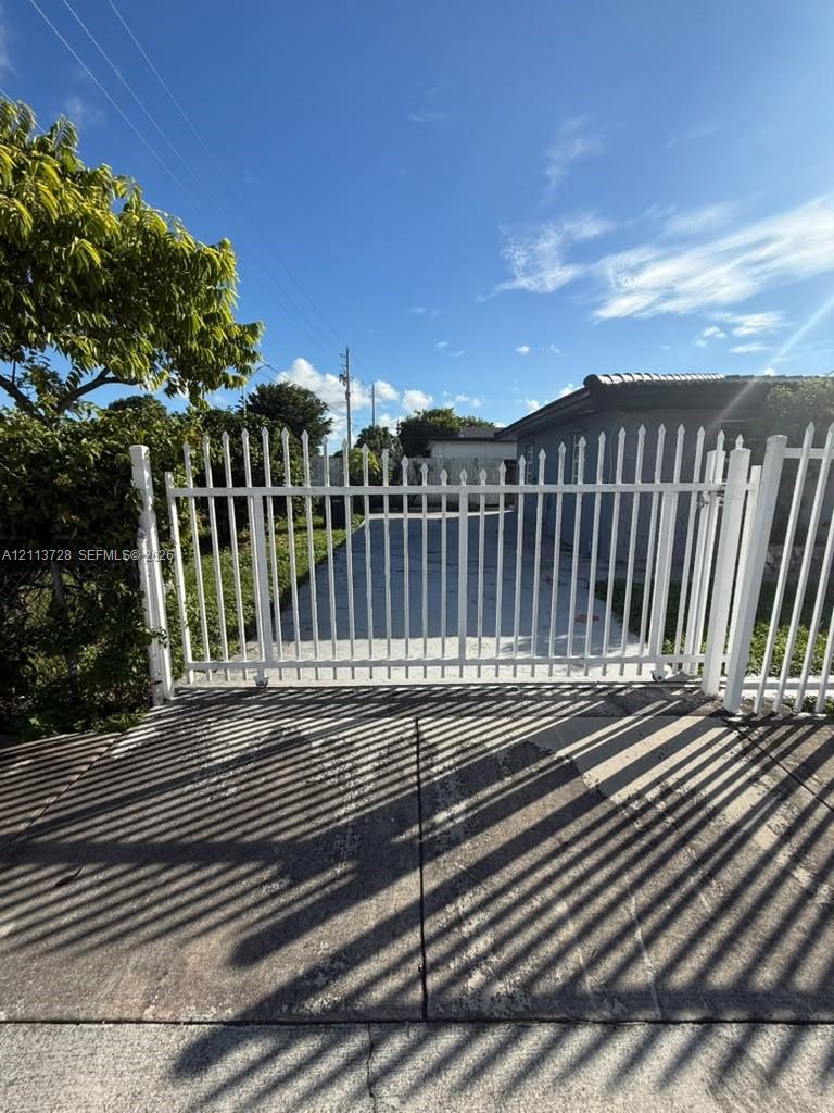 White metal picket gate with vertical bars and concrete driveway White metal picket gate with vertical bars and concrete driveway