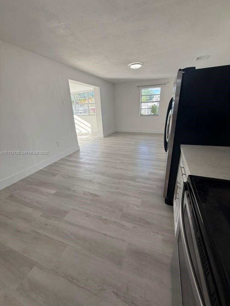 Light-toned wood-finish flooring, white cabinetry, light-colored countertops, and stainless steel appliances