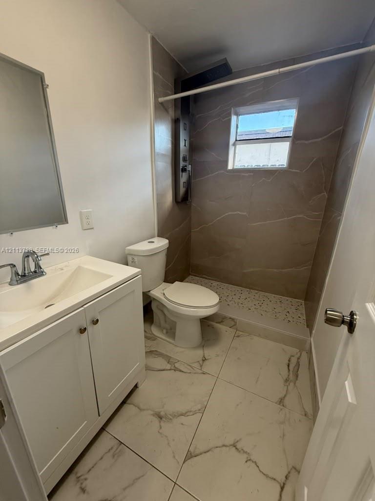 Bathroom featuring oversized floor tiles with stone-patterned veining, white vanity cabinet with a integrated sink, and a walk-in shower with large-format wall tiling and a pebble-texture floor base