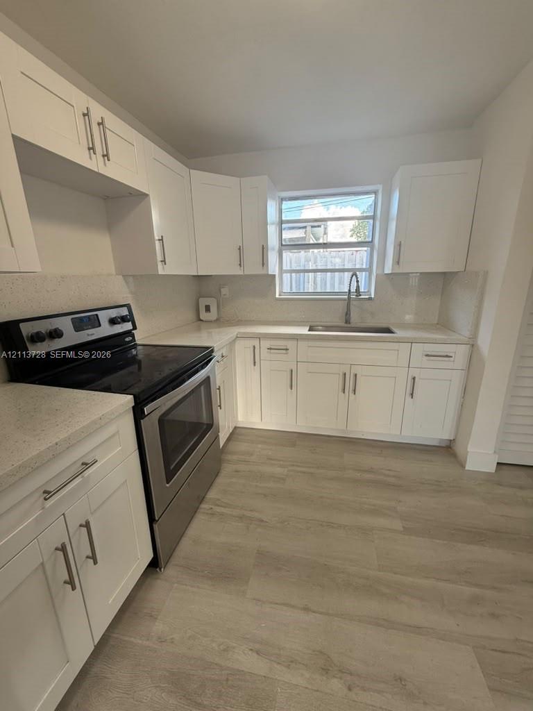 Kitchen featuring white Shaker-style cabinetry, light-toned stone-finish countertops, stainless steel appliances, wood-finish flooring, and a single-basin undermount sink with a pull-down faucet