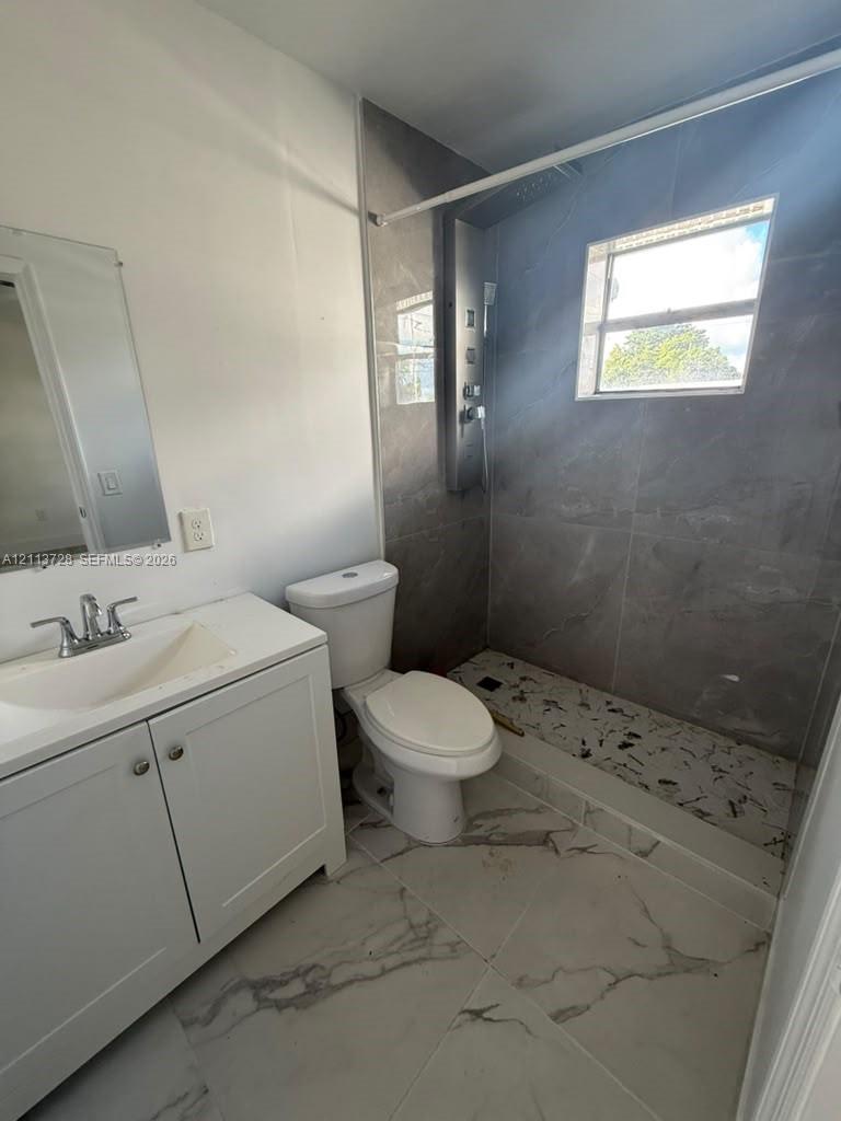 Bathroom featuring large-format tile flooring, a white vanity with an integrated sink, and a walk-in shower with full-height tile surround, a built-in shower panel system, and a pebble-stone basin floor