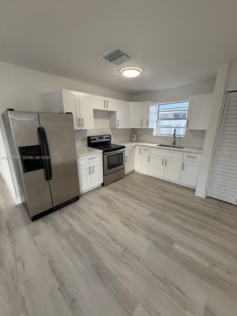 Kitchen featuring white shaker-style cabinetry, stainless steel appliances, light-toned stone countertops, and wood-finish flooring