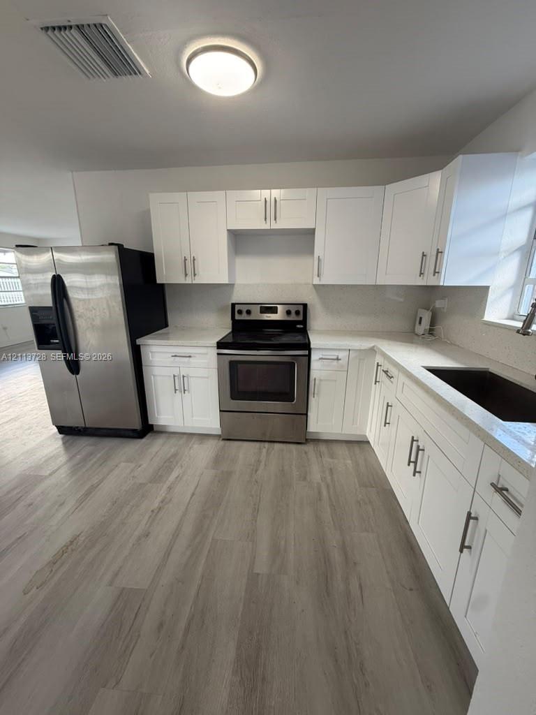 Kitchen featuring white shaker-style cabinetry, stainless steel appliances, light stone-finish countertops, and wood-finish flooring