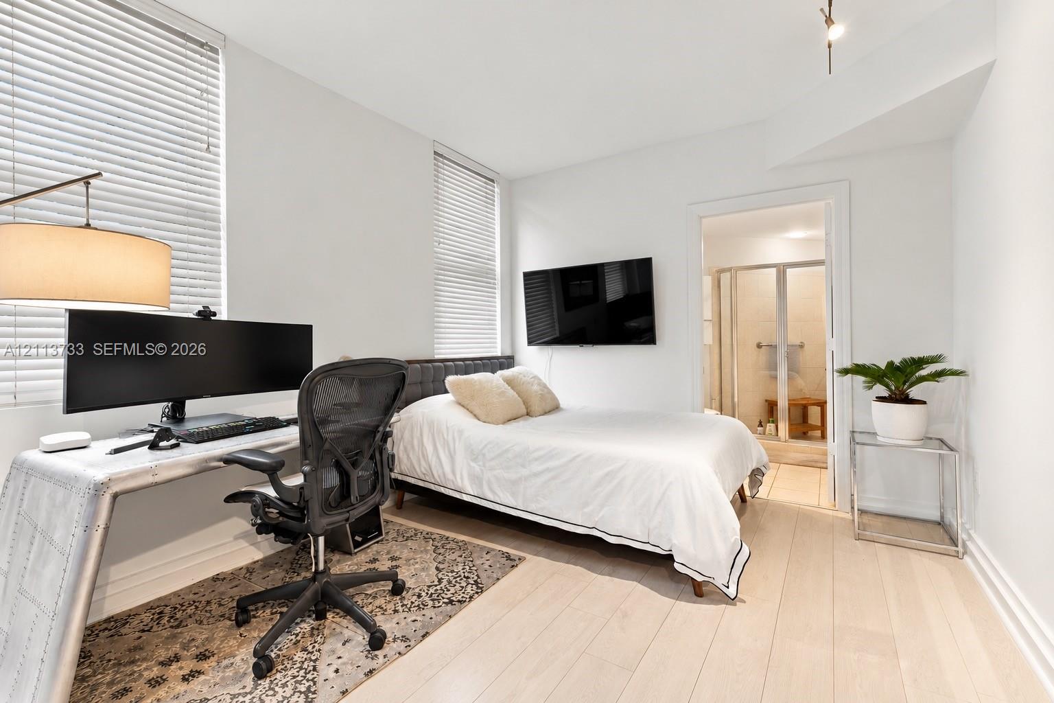 Light-filled room featuring wood-finish flooring, tall windows with horizontal blinds, and a neutral color palette