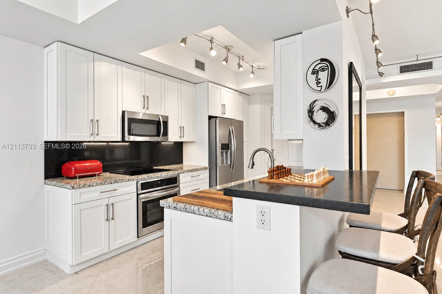 Kitchen featuring white shaker-style cabinetry, a stone-finish countertop, black backsplash, stainless steel appliances, and a breakfast bar with stone surfacing