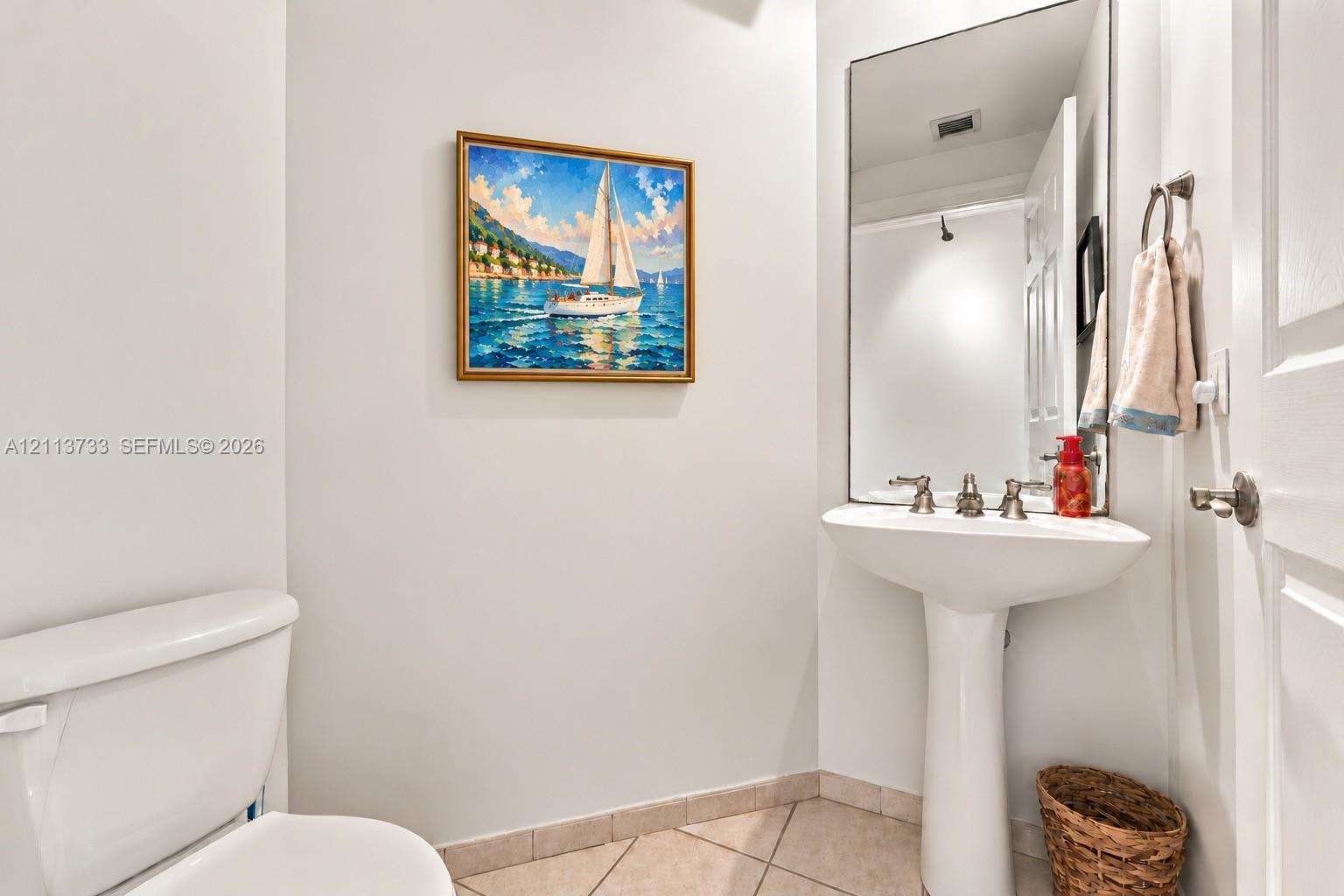 Powder Room: White pedestal sink with a metallic three-handle faucet, large wall-mounted mirror, and neutral-tone tile flooring
