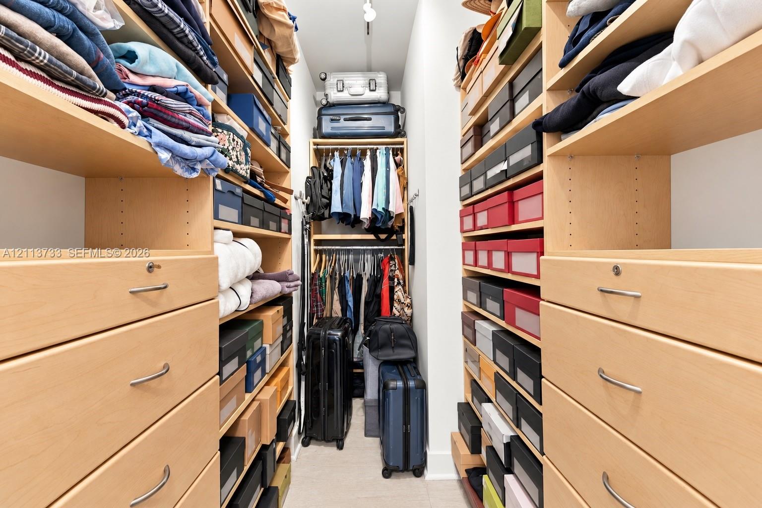 Custom reach-in closet featuring extensive built-in light wood cabinetry, multiple open shelving tiers, integrated drawers with metal hardware, and dual-level hanging rods