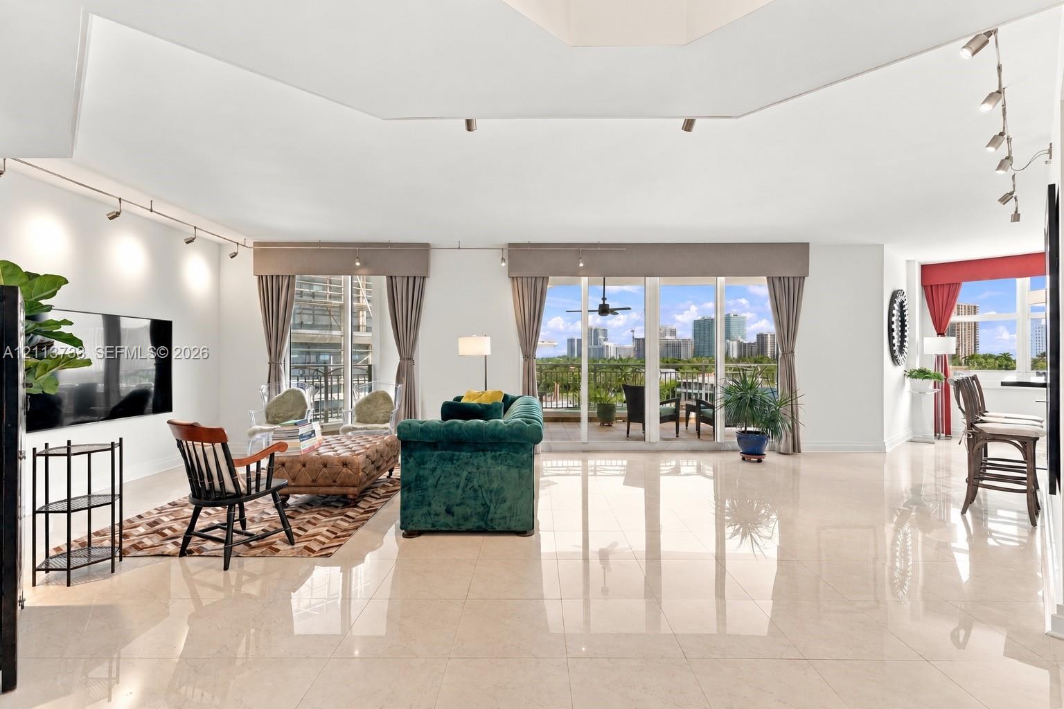 Spacious interior featuring high-gloss tile flooring, vaulted ceilings, adjustable track lighting, and multiple floor-to-ceiling glass panel doors providing access to a balcony