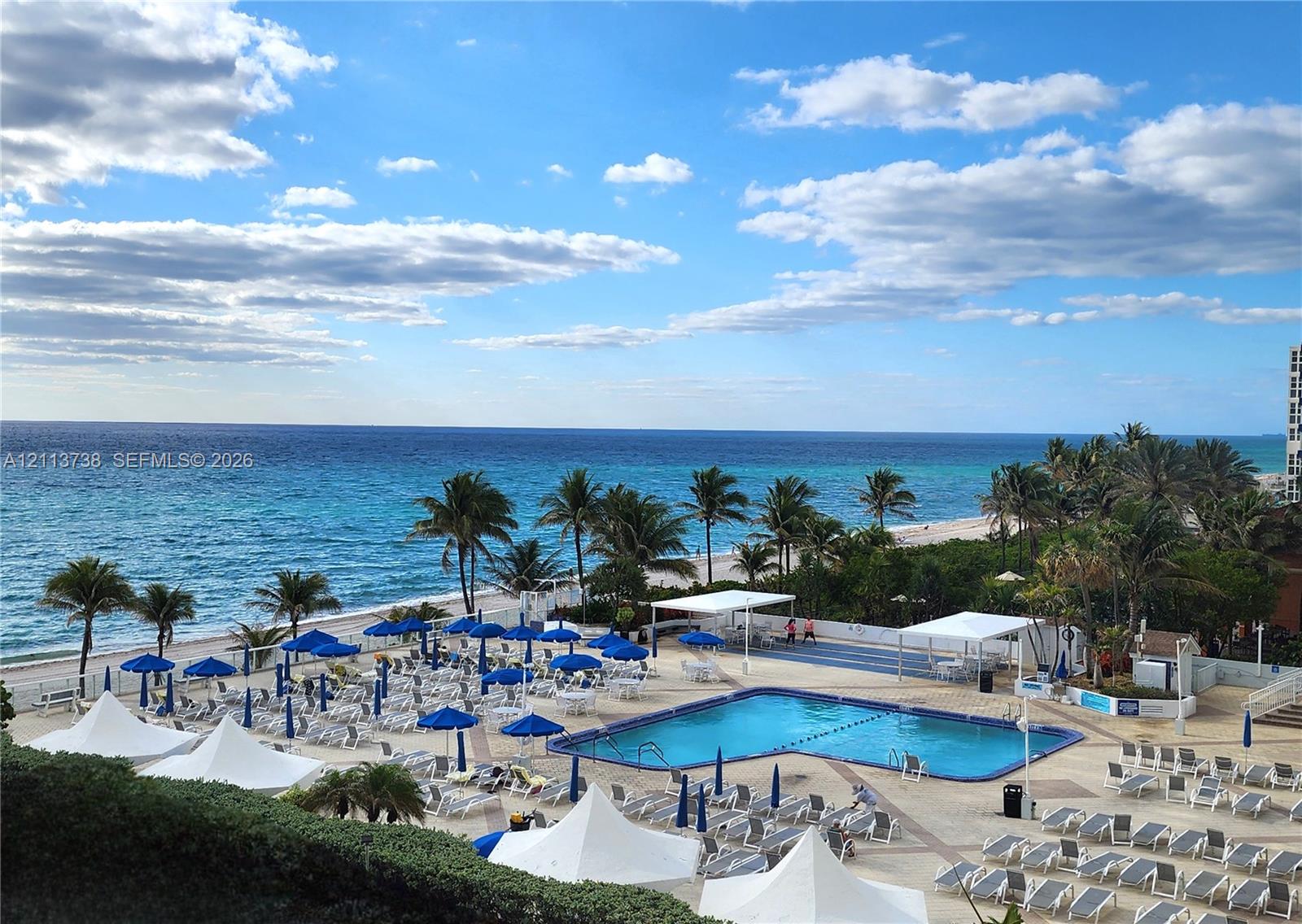 Swimming pool area featuring expansive stone deck, structured shade canopies, and private beach access