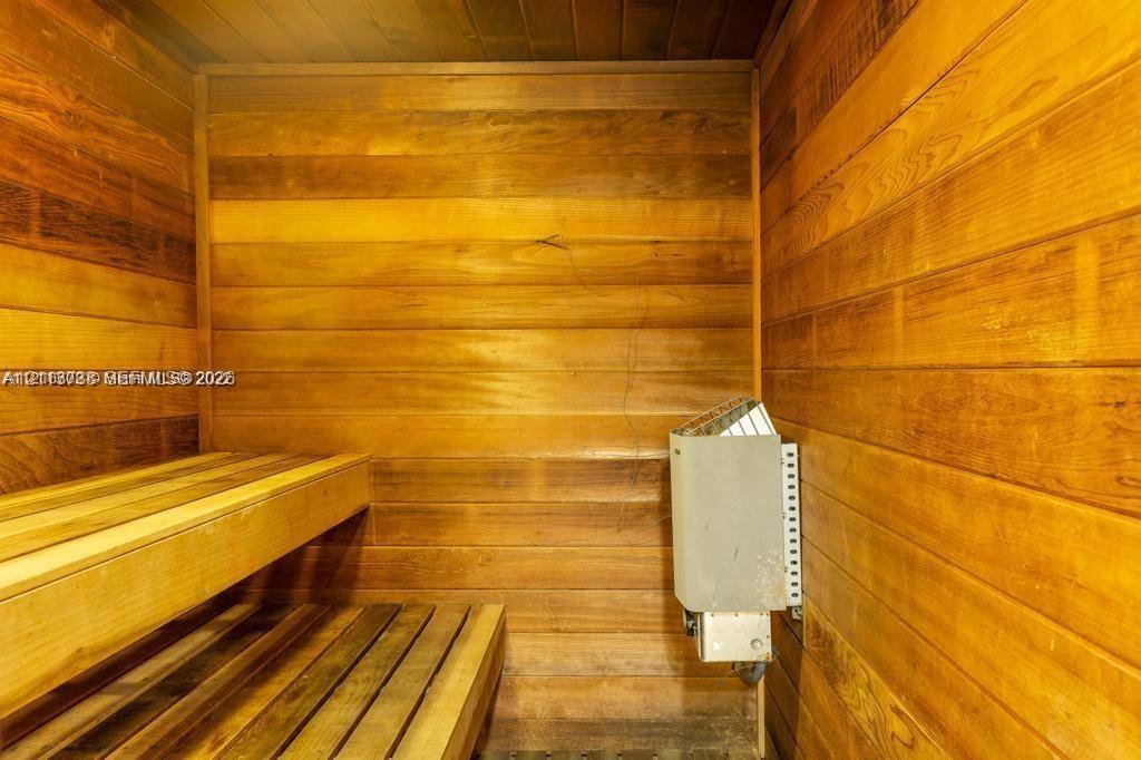 Sauna room featuring wood-paneled walls, multi-level slatted wood benches, and a wall-mounted electric heater