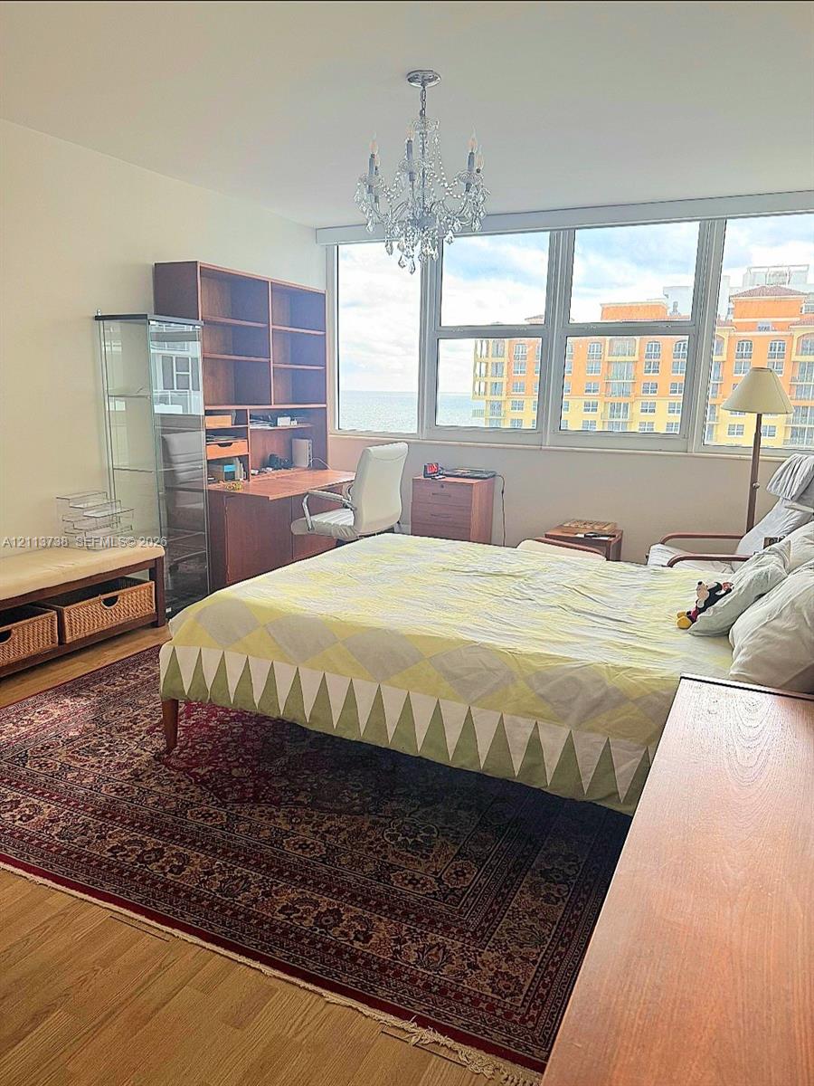 Floor-to-ceiling windows with coastal horizon backdrop, wood-finish flooring, and decorative crystal chandelier