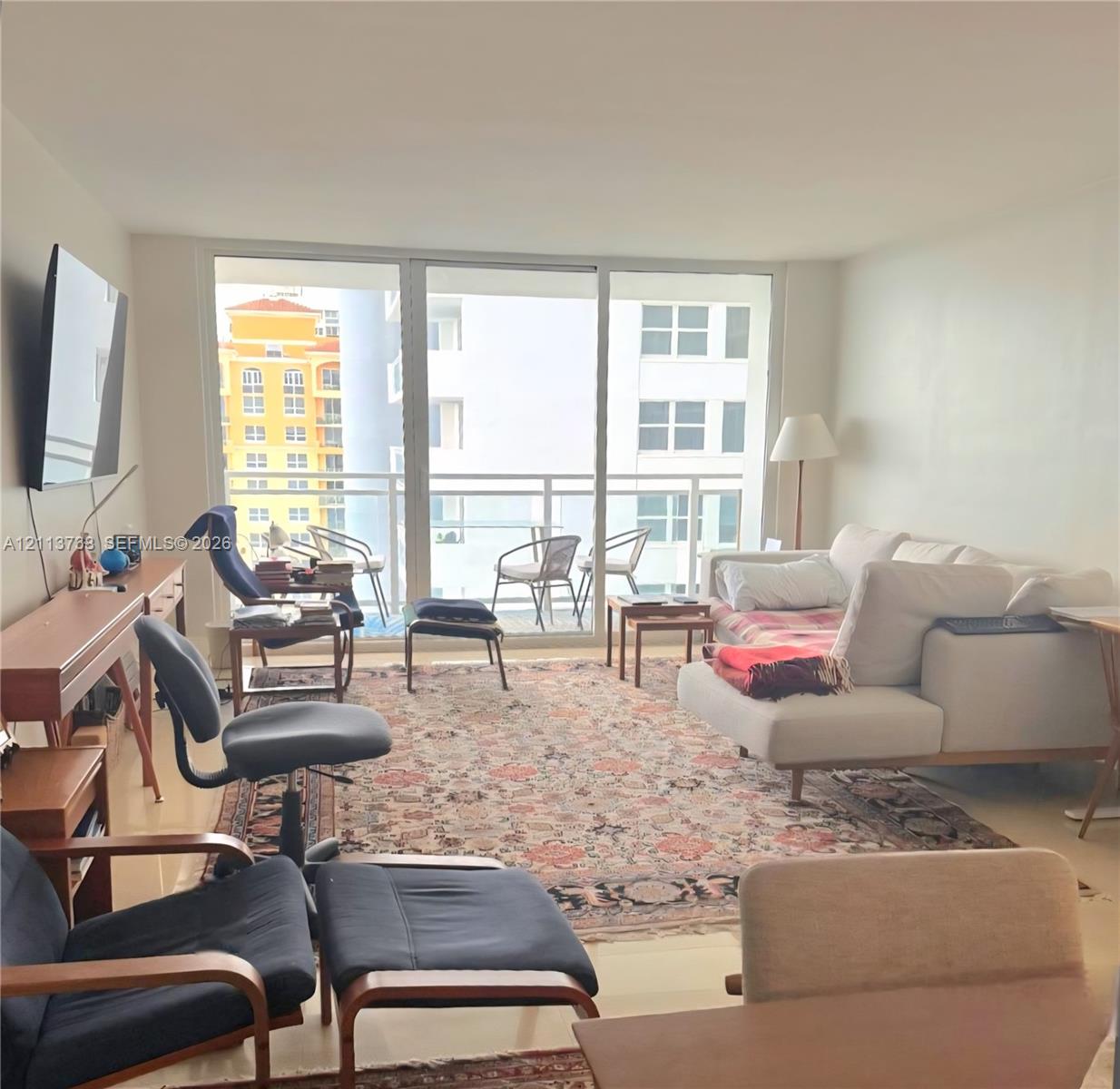 Floor-to-ceiling glass panel windows, neutral ceramic tile flooring, and a private balcony with metal railing