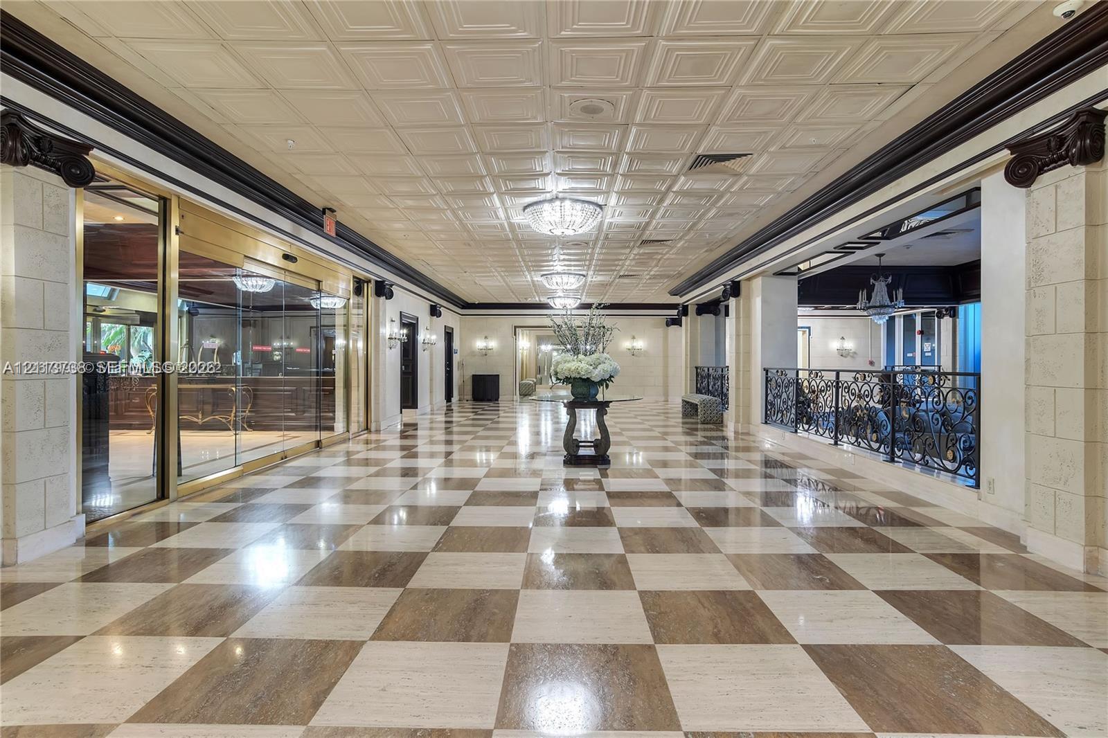 Grand lobby featuring a coffered ceiling, checkered marble flooring, decorative crown molding, ornamental column capitals, and ornate wrought-iron railings