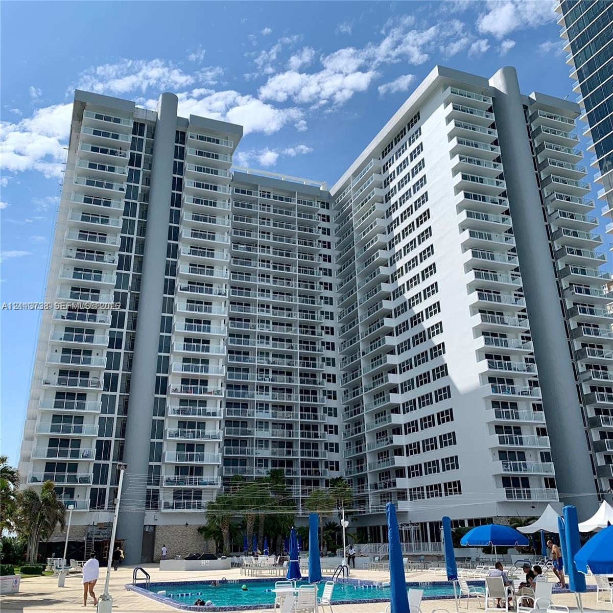 High-rise residential exterior featuring expansive private balconies, floor-to-ceiling glass windows, a swimming pool, and stone facade accents