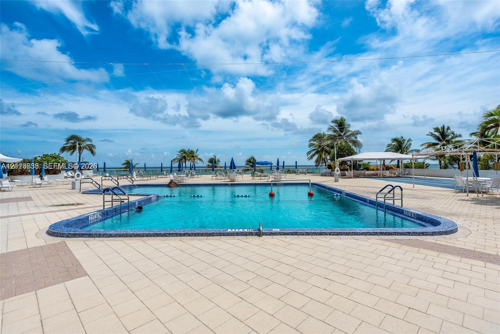 In-ground swimming pool featuring a tiled waterline, metal entry rails, and expansive paved pool deck