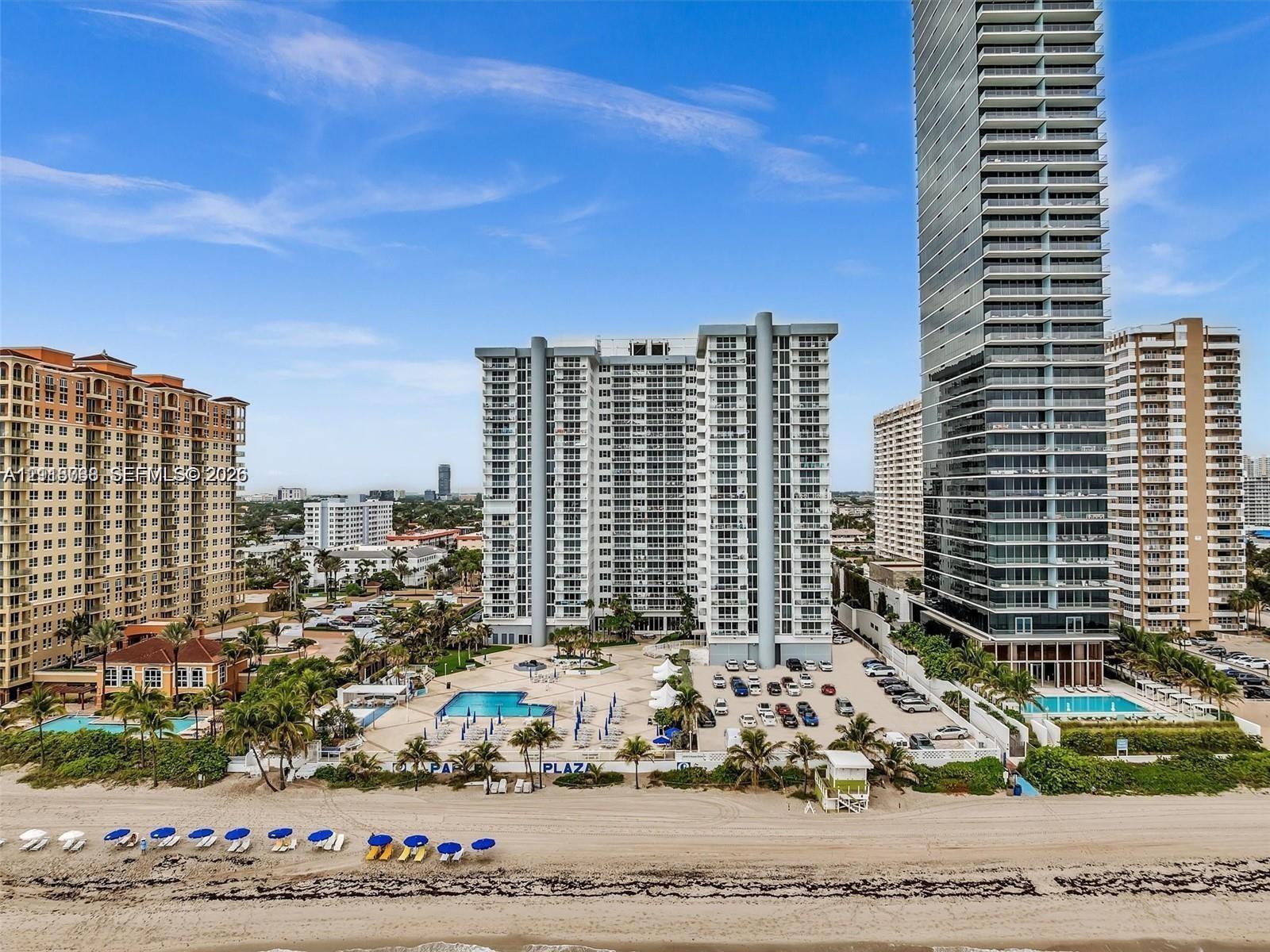High-rise beachfront property featuring direct beach access, multiple outdoor swimming pools, expansive paved sun decks, and mature palm landscaping
