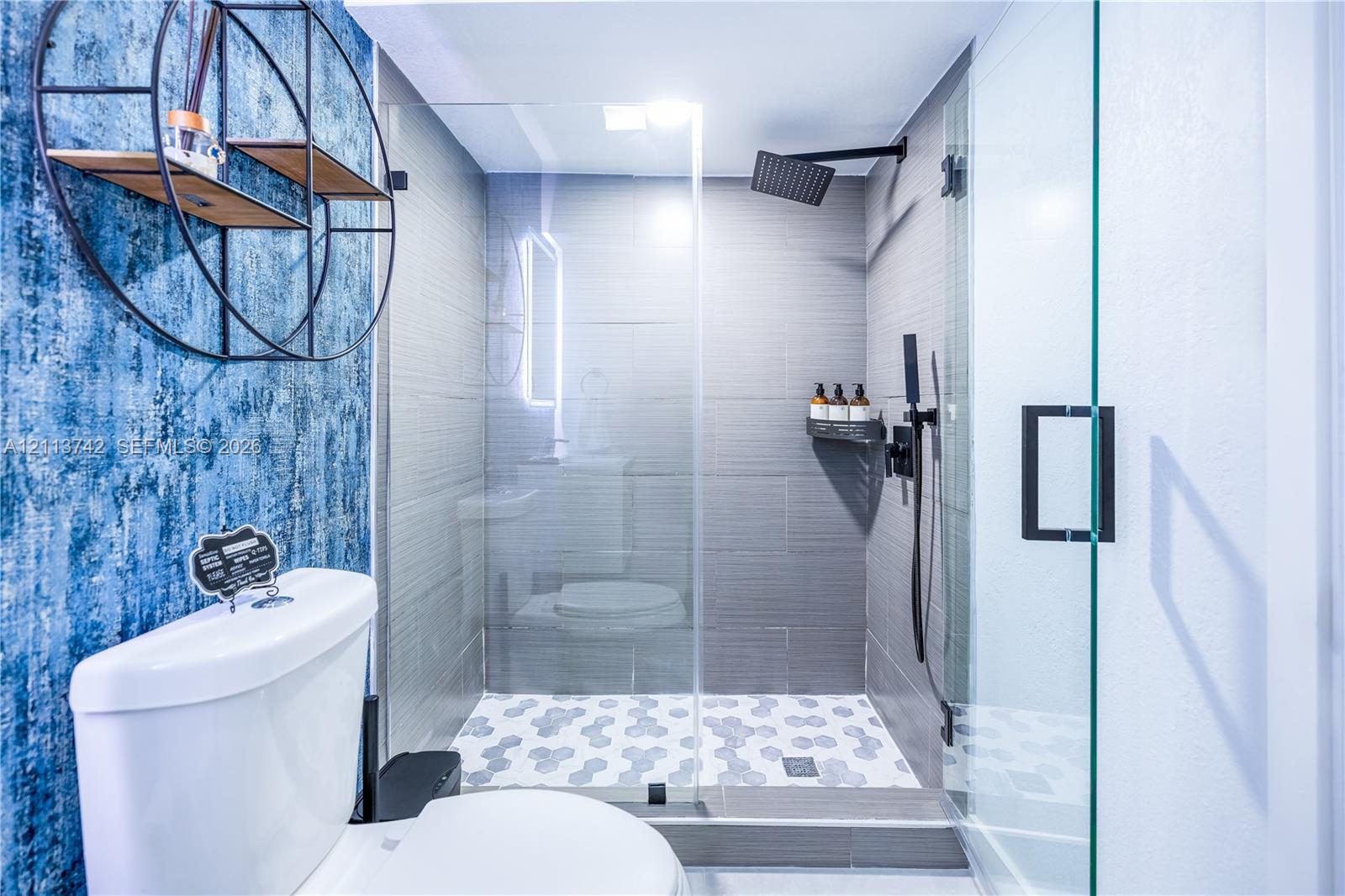 Walk-in glass-enclosed shower featuring large-format gray wall tile, geometric pattern floor tile, and matte black rainfall shower fixture