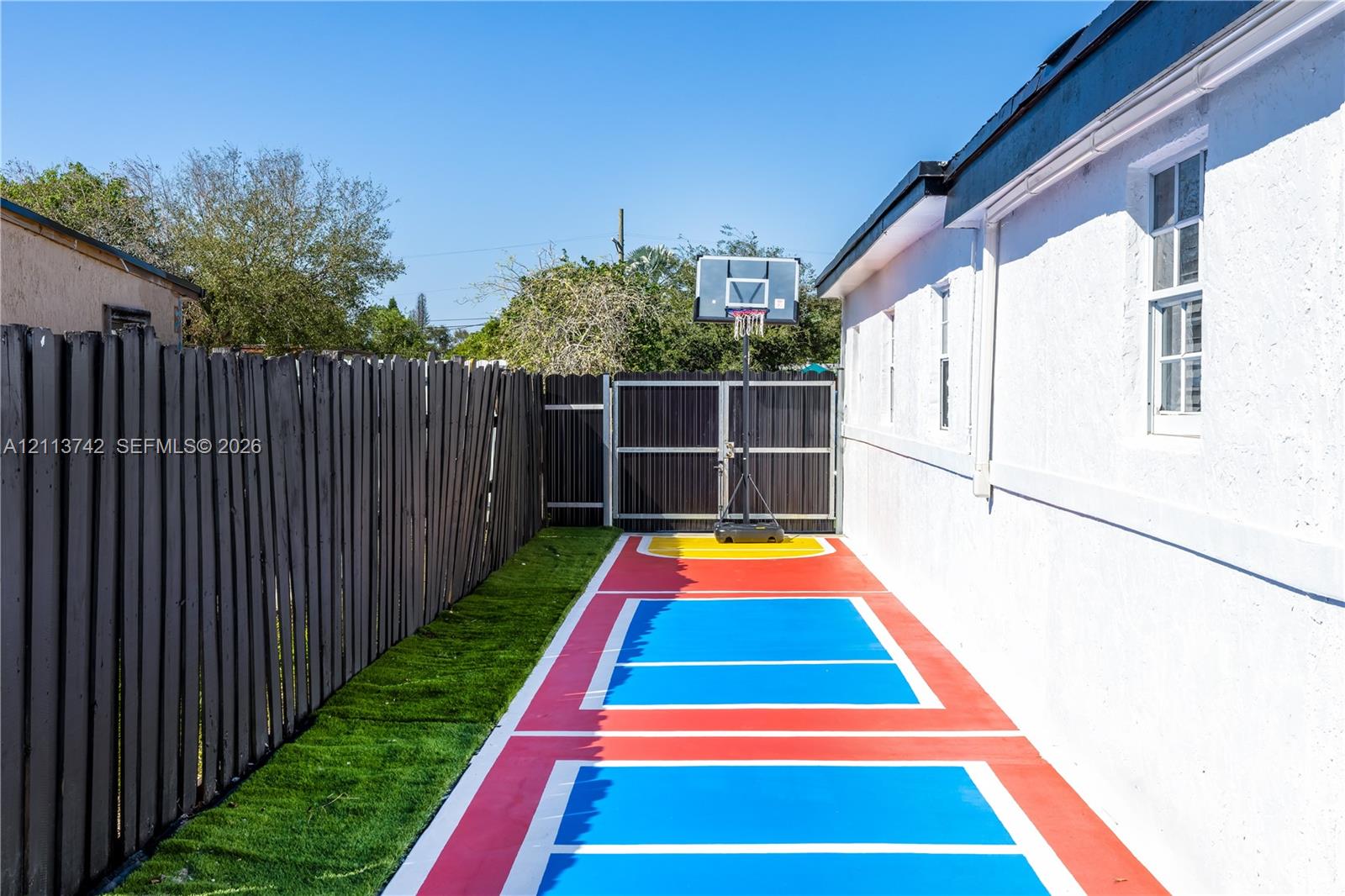 Side yard featuring a painted sports court, synthetic turf, wood-finish perimeter fencing, and a gated entrance
