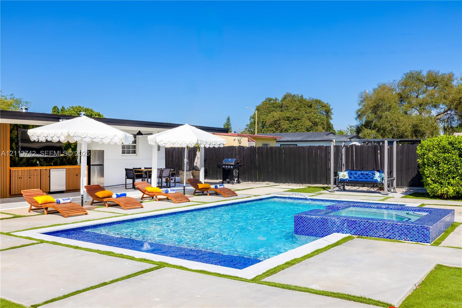 Outdoor living space featuring a swimming pool, integrated tiled spa, concrete paver decking, and built-in outdoor kitchen cabinetry