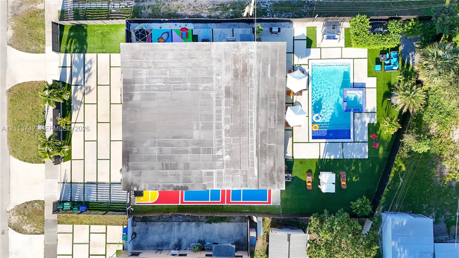 Aerial view of property featuring a swimming pool, integrated spa, multi-sport court, and paved patio surfaces with turf accents