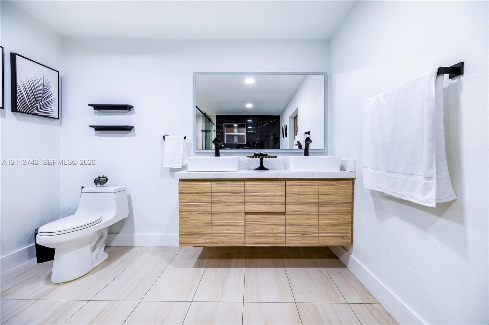 Floating wood-finish vanity with dual vessel sinks, stone-surface countertop, and matte black hardware