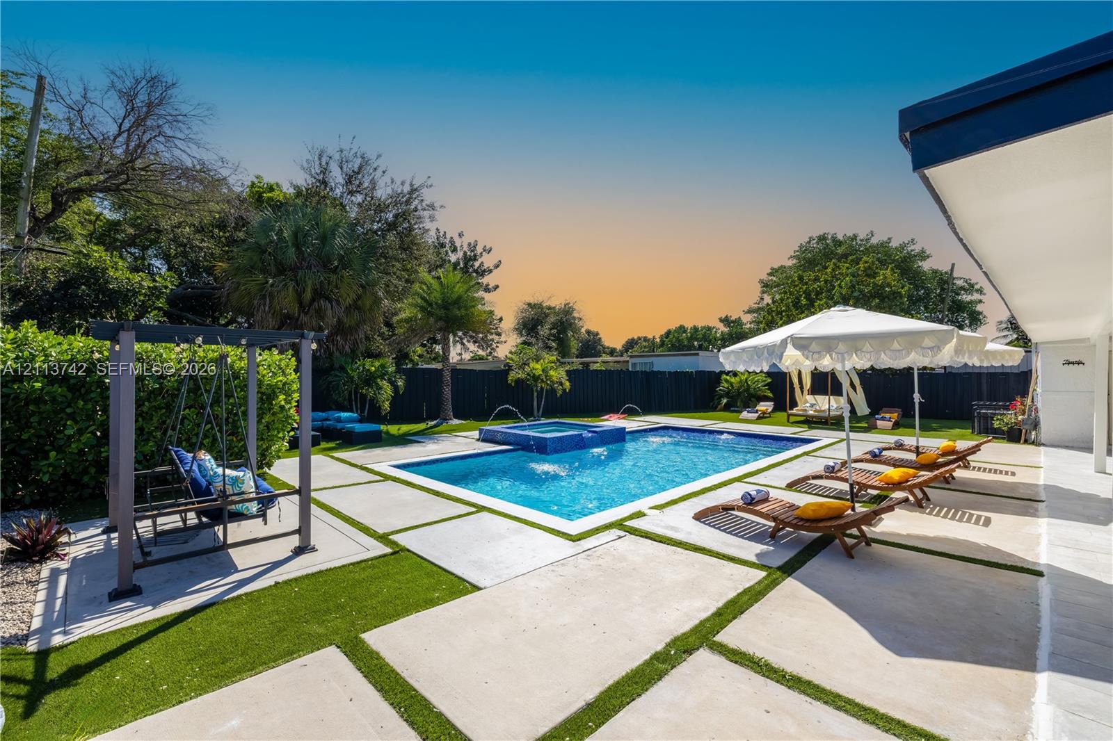 Rear yard featuring a rectangular swimming pool with an integrated spa, concrete paver decking, and perimeter privacy fencing