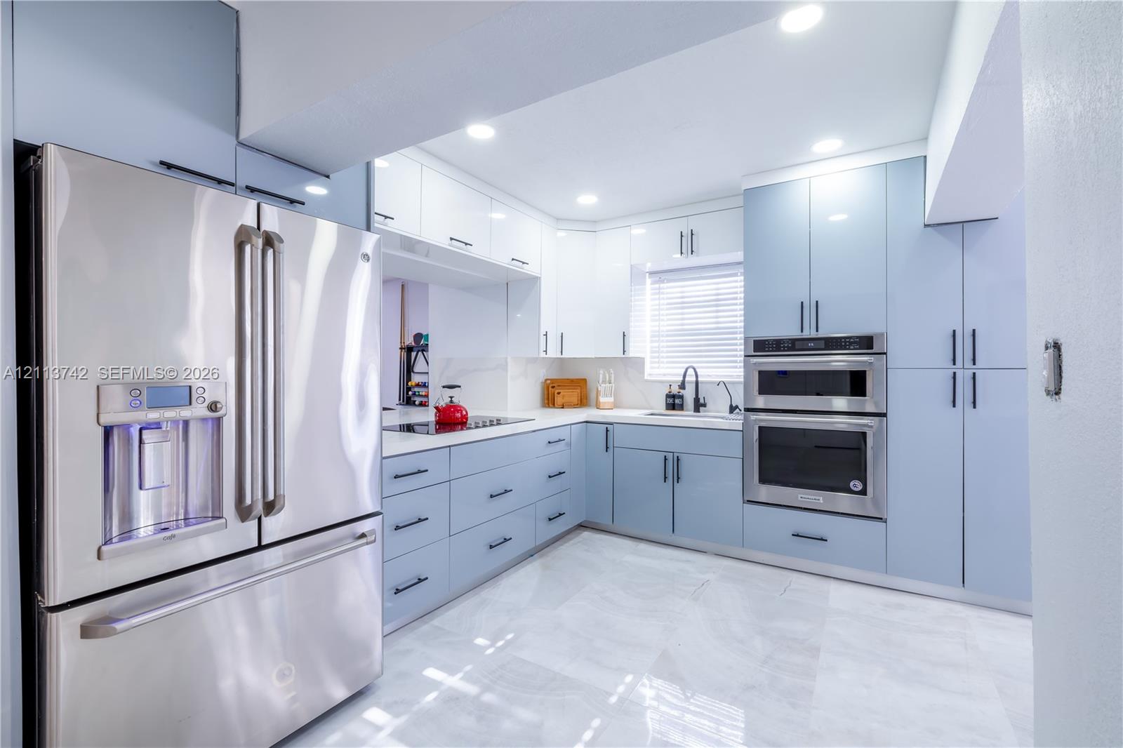 Kitchen featuring light blue and white slab-style cabinetry, stainless steel double wall oven, stainless steel refrigerator, stone-surface countertops, and light-toned tile flooring