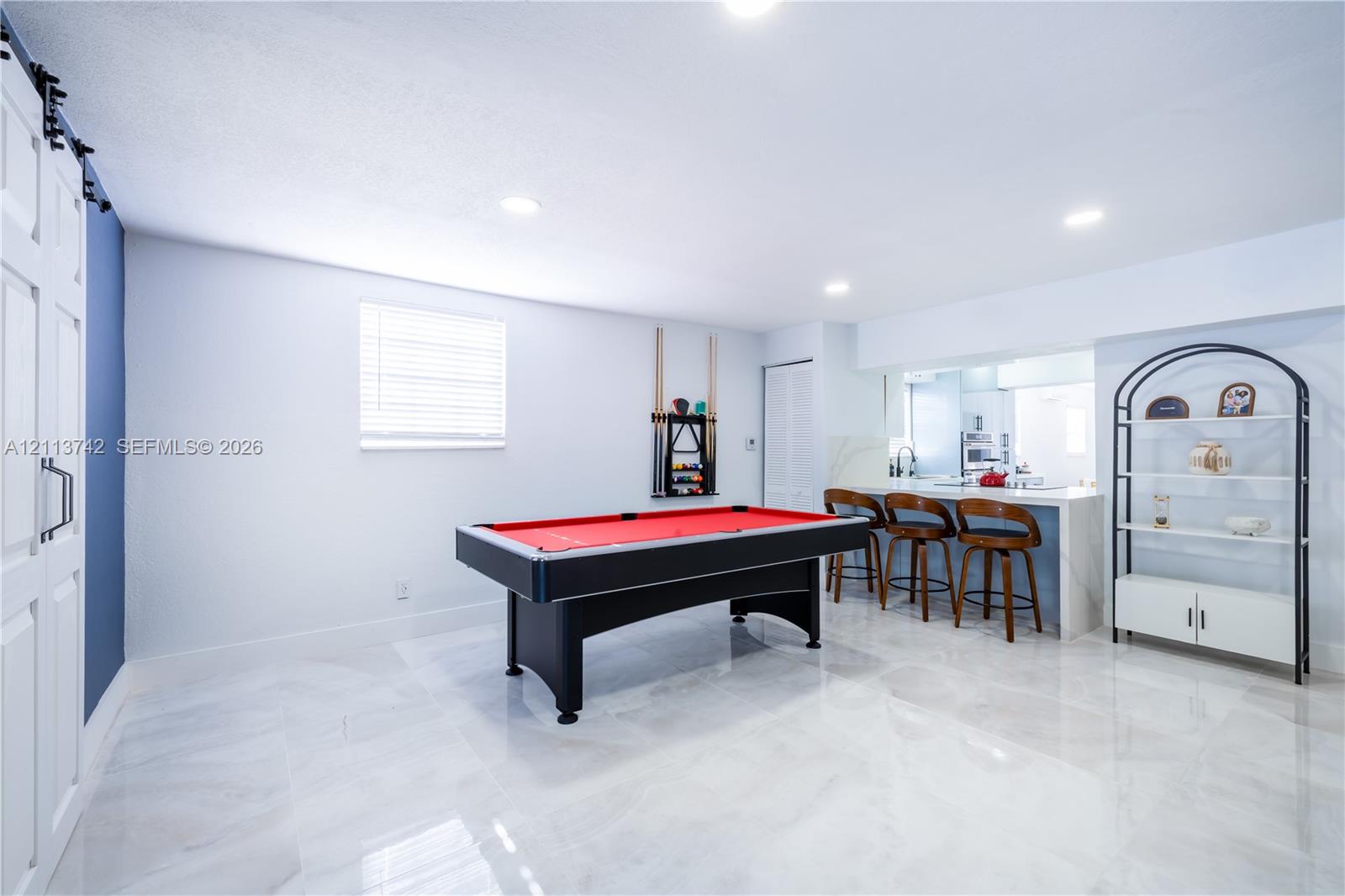 Polished large-format tile flooring, built-in breakfast bar with stone-finish countertop, sliding barn-style door, and recessed lighting