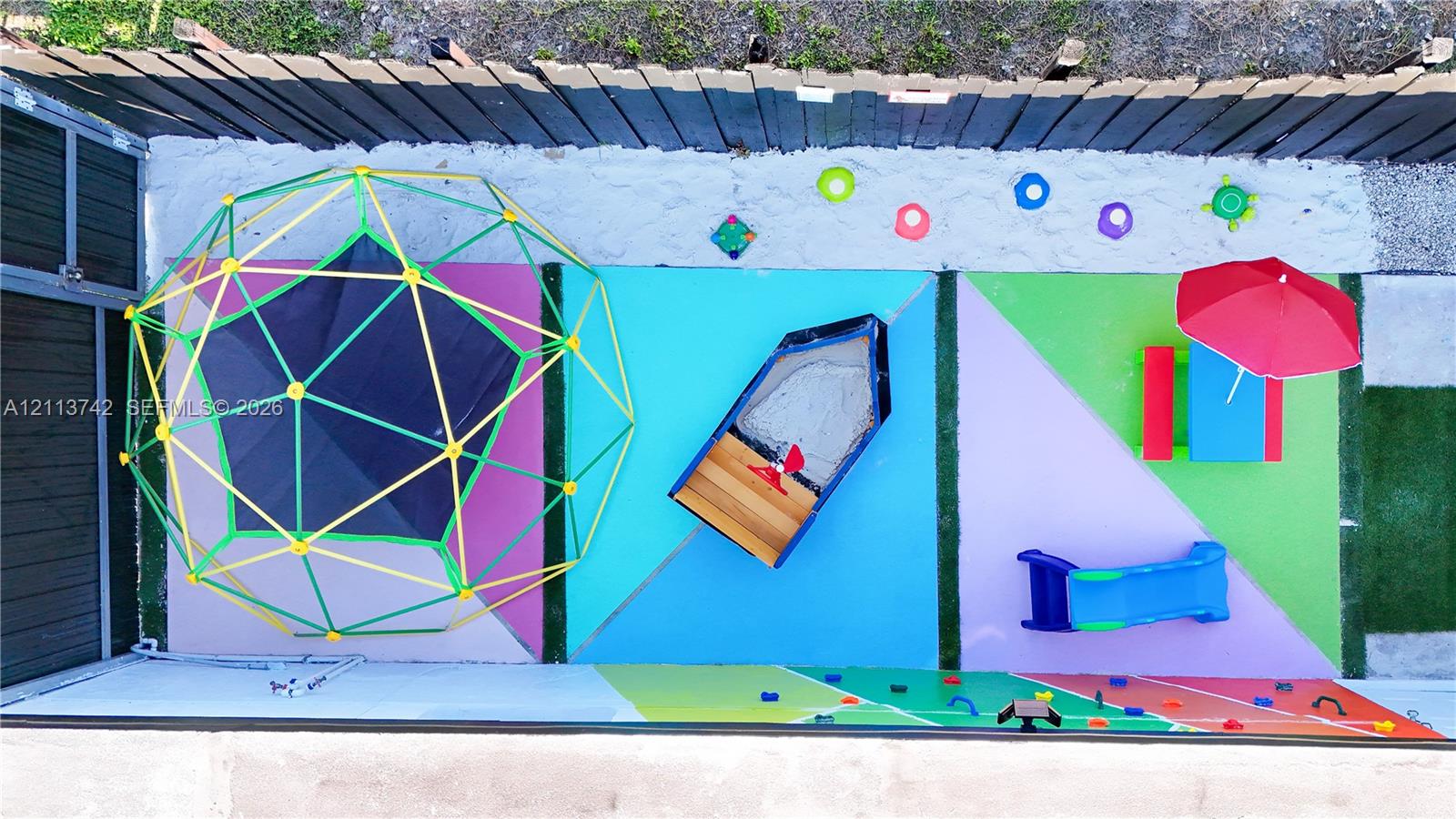 Fenced outdoor area featuring a sand pit and multi-colored poured-in-place rubberized surfacing