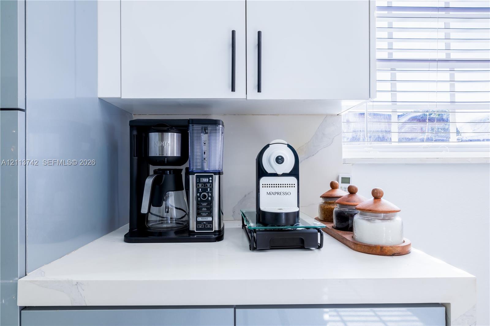 White shaker-style cabinetry with matte black hardware, stone-surface countertop with subtle veining, and integrated horizontal window blinds