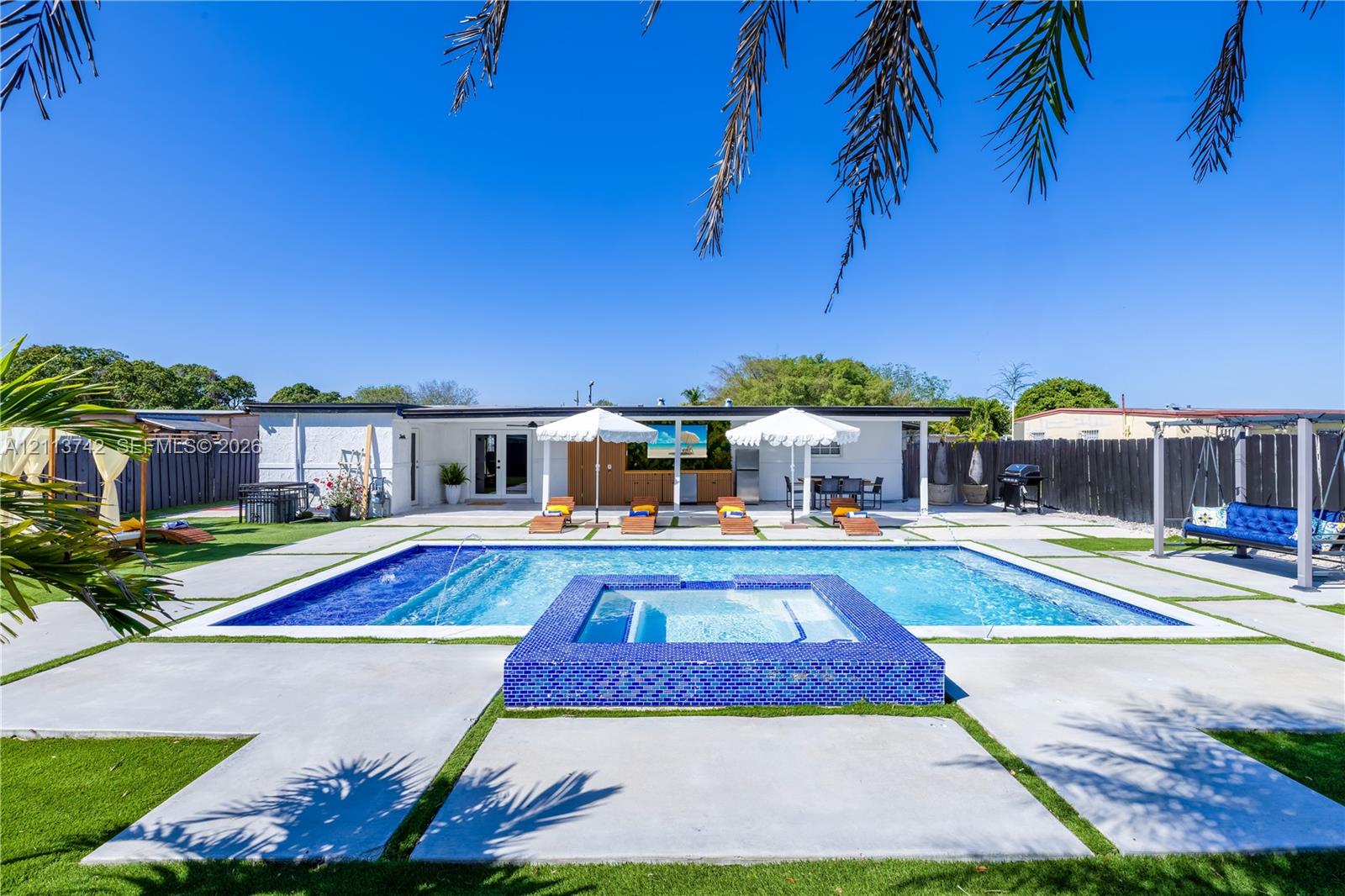 Backyard featuring an in-ground pool with a raised spa, blue tile surround, concrete paver decking, and artificial turf accents