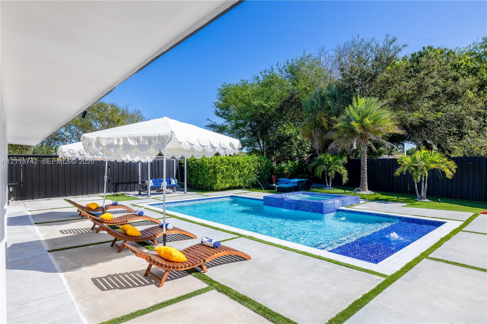 Swimming pool with integrated spa, blue mosaic tile accents, concrete paver patio with turf inlays, and perimeter privacy fencing Swimming pool with integrated spa, blue mosaic tile accents, concrete paver patio with turf inlays, and perimeter privacy fencing