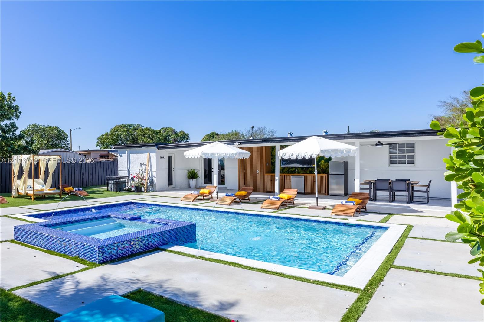 Backyard featuring a swimming pool with a raised tiled spa, expansive concrete paver decking, and a covered outdoor kitchen area
