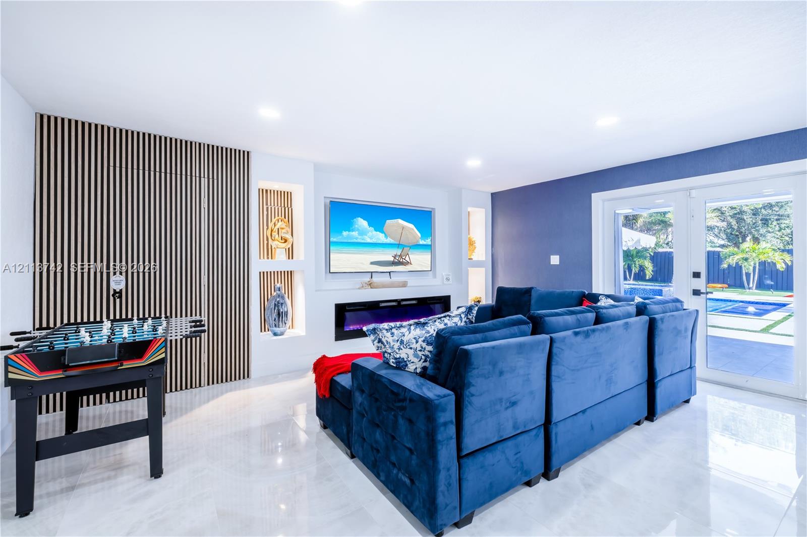 Living area featuring large-format tile flooring, recessed lighting, a linear electric fireplace, built-in shelving, and vertical wood-slat wall accents